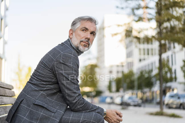 Portrait of fashionable mature businessman sitting on a bench in the city — Stock Photo