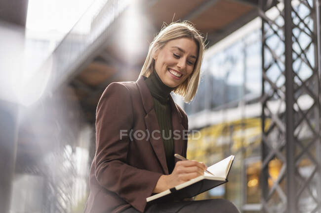 Joven empresaria sonriente tomando notas en la ciudad - foto de stock