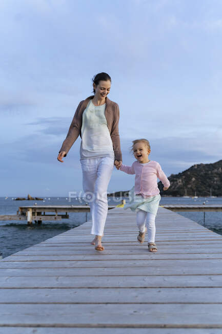Щаслива мати з дочкою йде по пристані на заході сонця. — стокове фото