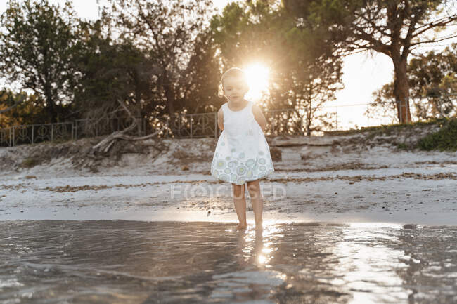Menina bonito criança de pé na praia ao pôr do sol — Fotografia de Stock