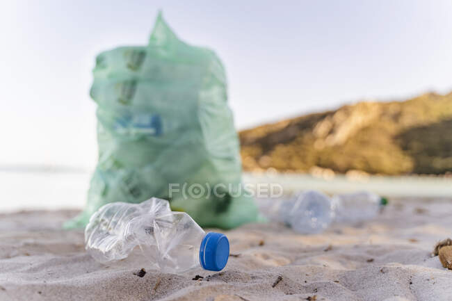 Пустые пластиковые бутылки и мусорный бак полный собранных пластиковых бутылок на пляже — стоковое фото