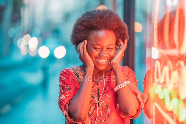 Giovane donna sorridente con cuffie in piedi accanto alla luce al neon — Foto stock