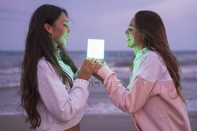Deux amies heureuses tenant la lumière menée sur la plage la nuit — Photo de stock