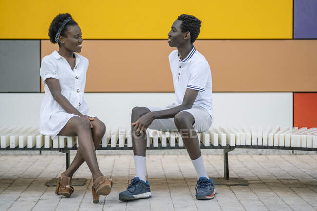 Jeune couple souriant assis sur un banc se regardant — Photo de stock
