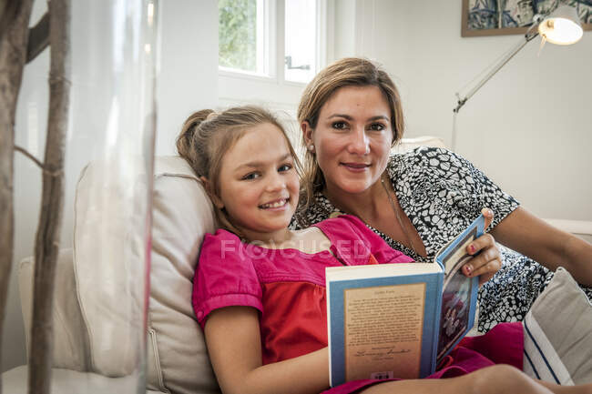 Ritratto di madre e figlia sorridente con libro sul divano in soggiorno — Foto stock