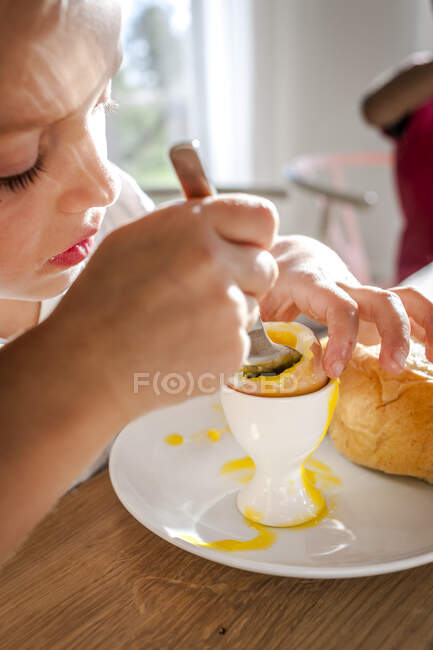 Chica comiendo un huevo hervido en la mesa de comedor - foto de stock