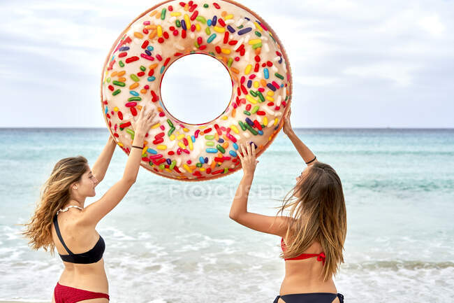 Due giovani donne in piedi di fronte al mare che tengono in alto un grande anello gonfiabile — Foto stock