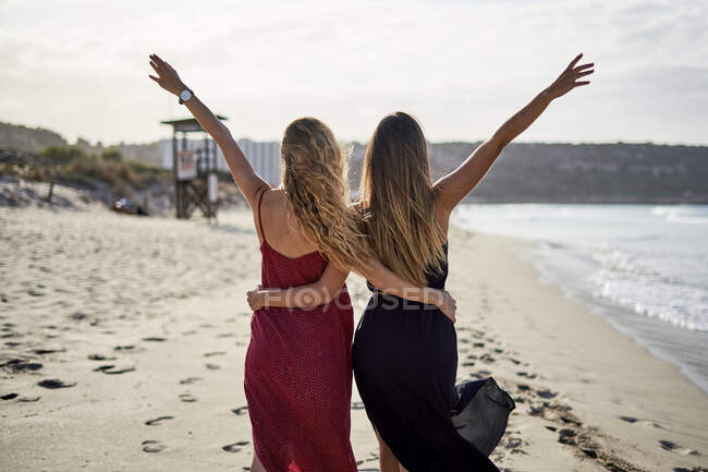 Zwei junge Frauen stehen Arm in Arm an einem Strand mit ausgestreckten Armen — Stockfoto