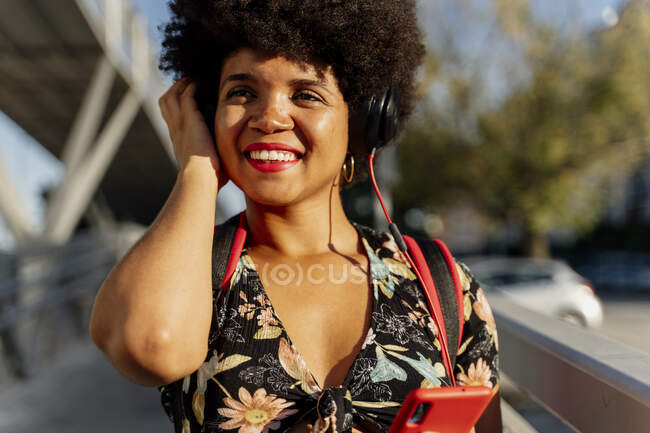 Mujer afroamericana con auriculares y smartphone escuchando música, mirando hacia los lados - foto de stock