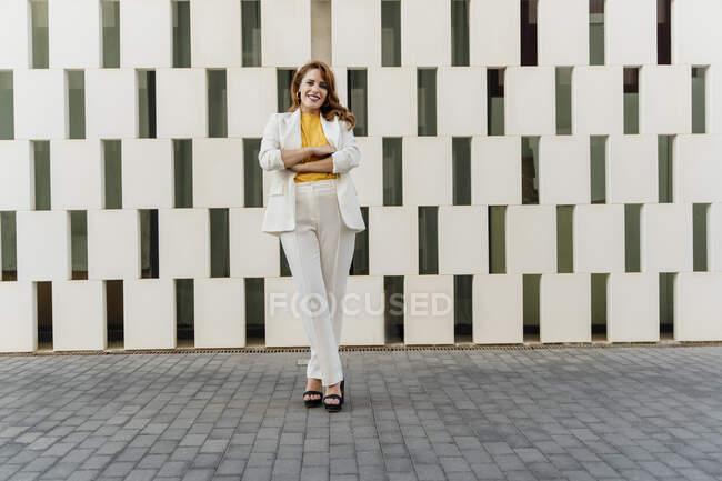 Femme d'affaires en pantalon blanc, debout devant la façade, les bras croisés — Photo de stock