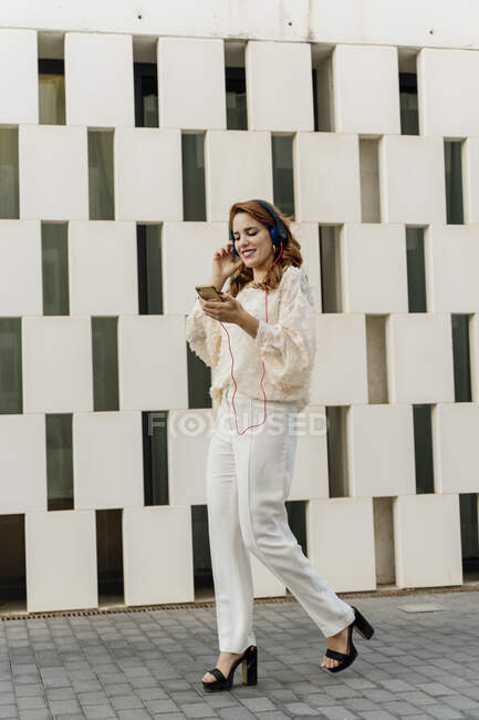 Donna d'affari che cammina per strada, ascoltando musica dal suo smartphone con le cuffie — Foto stock