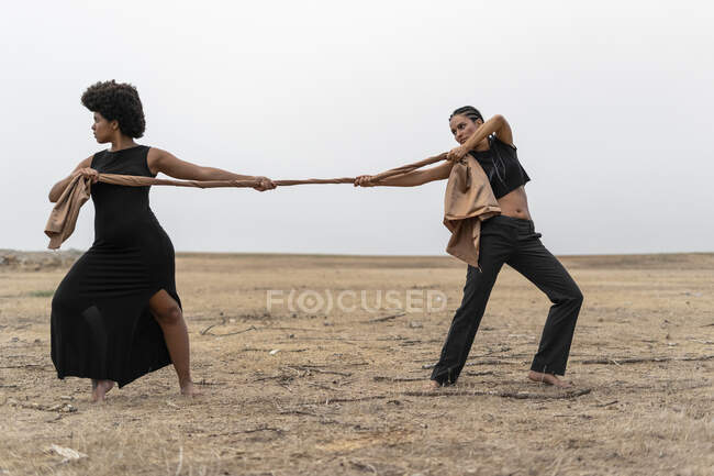 Dos mujeres tirando de un paño en un paisaje sombrío - foto de stock