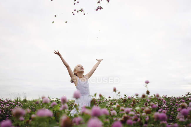Chica de pie en el campo de trébol, lanzando flores - foto de stock