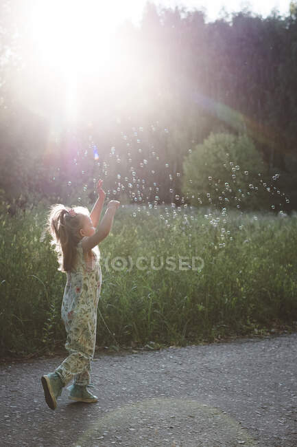Маленькая девочка ловит мыльные пузыри на солнце — стоковое фото