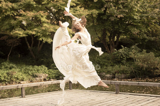 Bailarina vestindo vestido branco e pulando no molhe de madeira — Fotografia de Stock