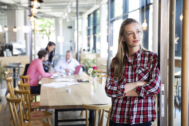 Retrato de una mujer de negocios casual en un café con colegas que tienen una reunión en segundo plano - foto de stock