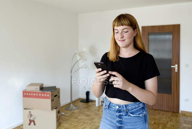 Porträt einer lächelnden jungen Studentin, die während des Umzugs ihr Smartphone benutzt — Stockfoto