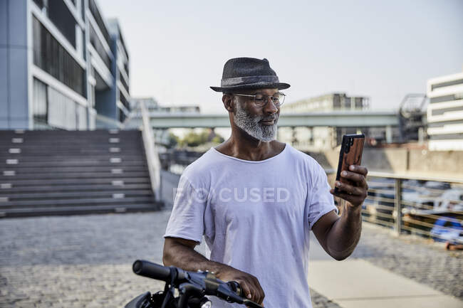 Портрет усміхненого дорослого чоловіка з E-Scooter, який дивиться на мобільний телефон. — стокове фото