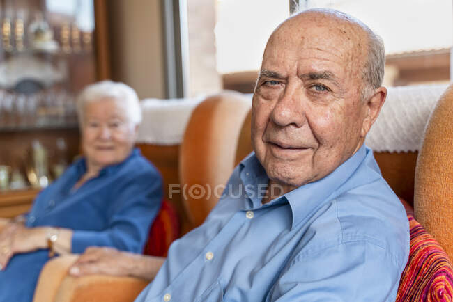 Літній чоловік з дружиною сидять у кріслі у вітальні. — стокове фото