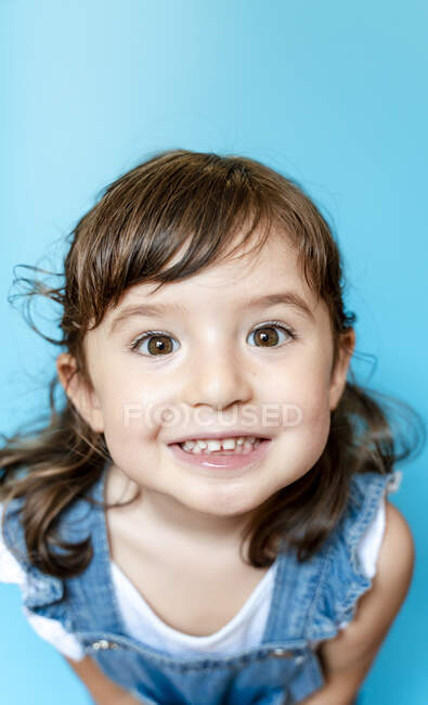 Portrait de mignonne petite fille souriante très expressive sur fond bleu — Photo de stock