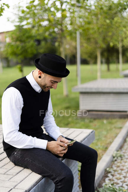 Homme élégant assis sur le banc à l'extérieur regardant le téléphone portable — Photo de stock