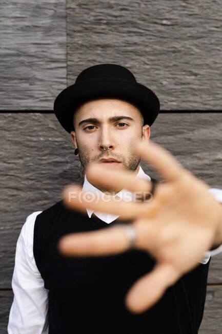 Retrato de un joven serio con piercing en la nariz y pendientes levantando la mano - foto de stock