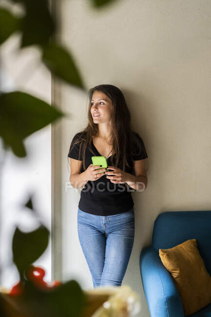 Young woman leaning against a wall holding cell phone — Stock Photo