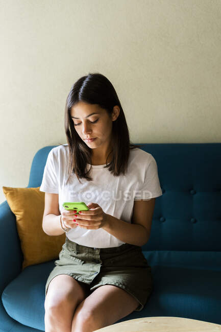 Молода жінка сидить на дивані з мобільним телефоном. — стокове фото