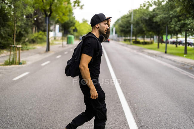 Молодой человек с рюкзаком переходит улицу в городе — стоковое фото