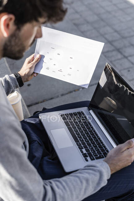 Man sitting outdoor using laptop and reviewing paper — Stock Photo