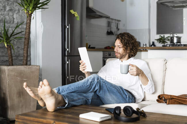 Relaxed man sitting on couch at home using tablet — Stock Photo