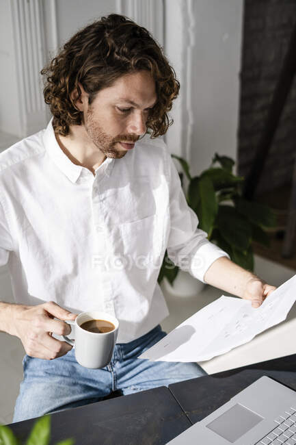 Чоловік сидить за столом вдома рецензуючи документи — стокове фото