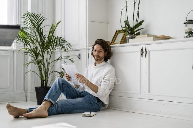 Портрет чоловіка, що сидить на підлозі вдома оглядає документи — стокове фото
