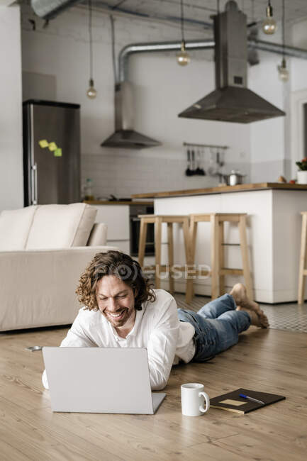 Усміхнений чоловік лежить на підлозі вдома, використовуючи ноутбук — стокове фото