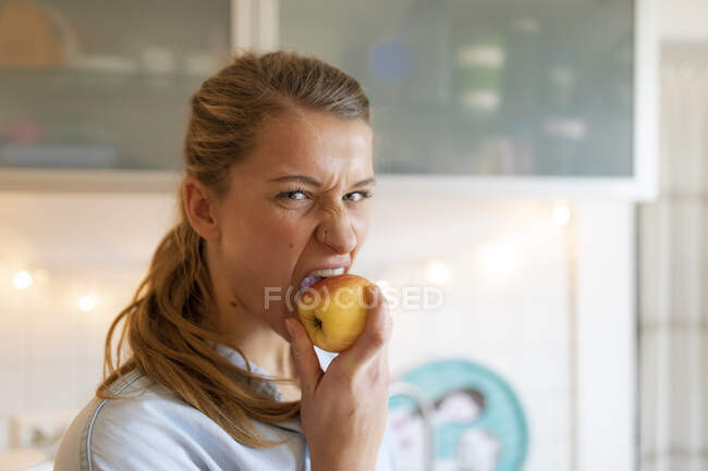 Портрет молодої жінки, що їсть яблуко вдома. — стокове фото