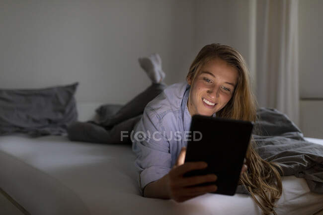 Felice giovane donna sdraiata a letto a casa di notte utilizzando tablet — Foto stock