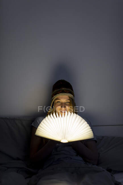 Giovane donna che legge libro illuminato a letto a casa — Foto stock