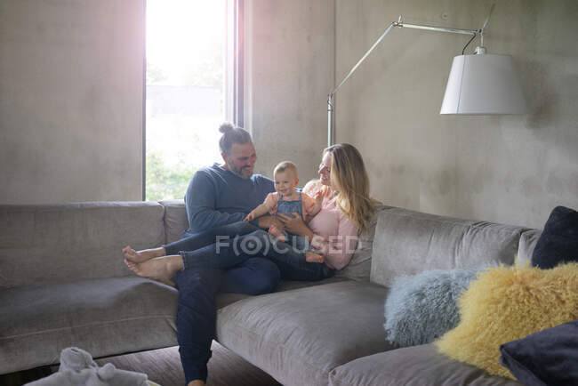Счастливая семья из трех человек сидит дома на диване — стоковое фото