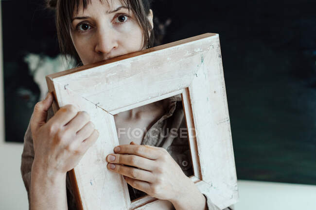 Portrait of a female painter in her studio holding picture frame — Stock Photo