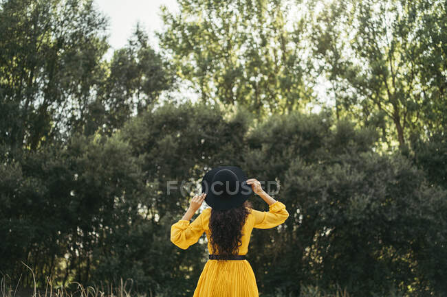 Vista posteriore di una giovane donna con cappello nero e vestito giallo godersi la natura — Foto stock
