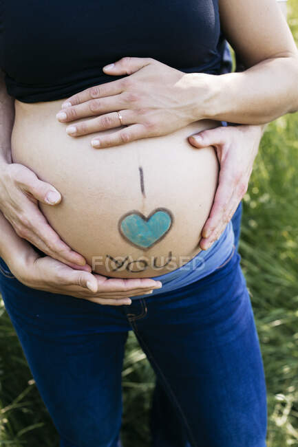 Les mains des futurs parents caressant le ventre du bébé à l'extérieur — Photo de stock