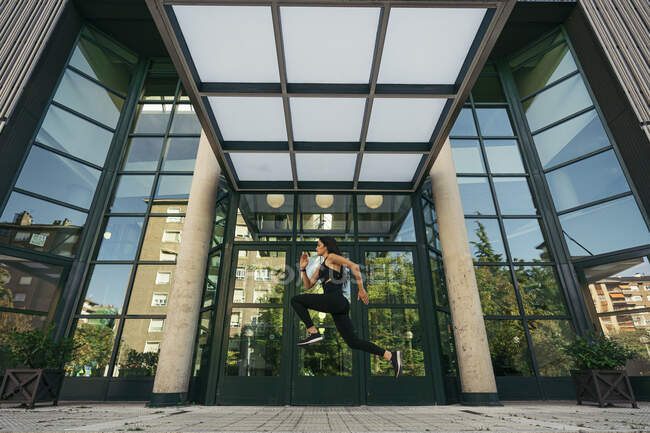 Giovane jogger femminile che salta davanti all'ingresso di un edificio — Foto stock