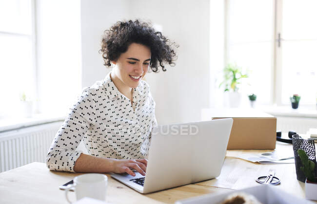 Улыбающаяся молодая женщина, работающая на ноутбуке за столом — стоковое фото