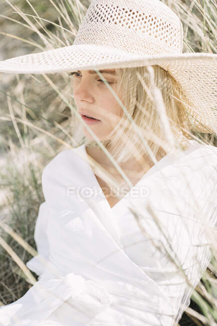 Portrait of blond young woman in dunes wearing white wrap blouse and summer hat — Stock Photo
