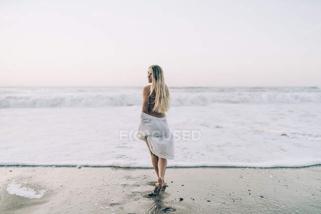 Giovane donna bionda in bikini e vestito bianco in spiaggia al mattino — Foto stock