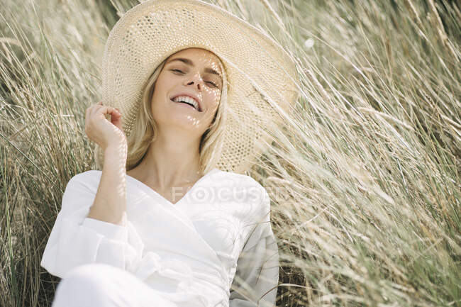 Ritratto di giovane donna bionda in dune da spiaggia con camicetta bianca e cappello estivo — Foto stock