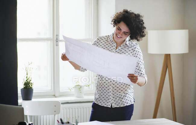 Smiling young woman studying a plan in office — Stock Photo