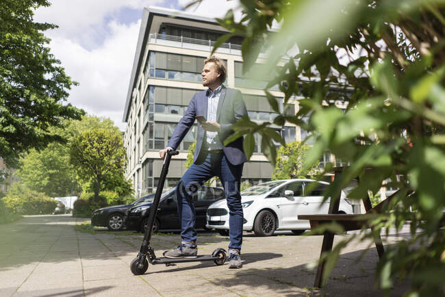 Uomo d'affari con E-Scooter e smartphone sul marciapiede della città — Foto stock