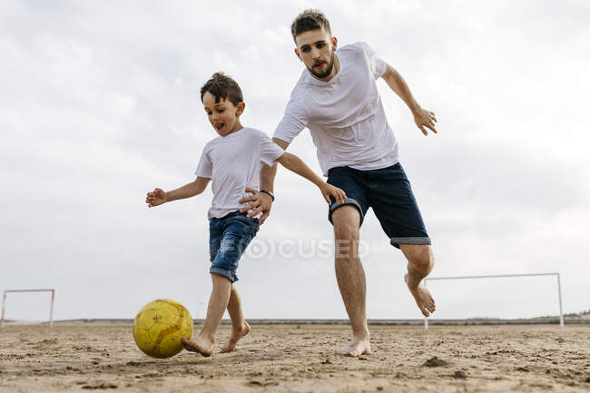 Ragazzo e uomo che giocano a calcio sulla spiaggia — Foto stock
