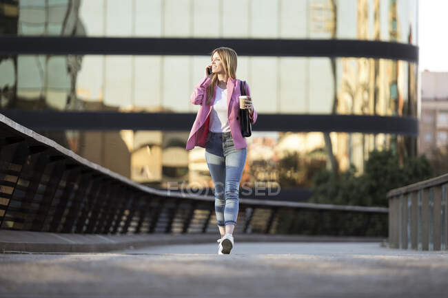 Молодая деловая женщина, используя смартфон и держа кофе, чтобы пойти — стоковое фото
